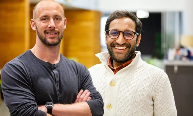 Two men smiling, one with a bald head and beard, the other with glasses and a beard.