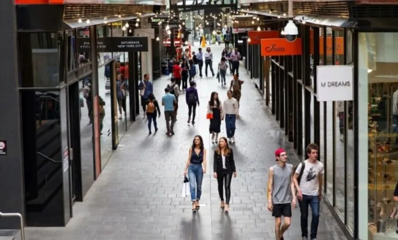 People walking through a modern indoor shopping arcade with storefronts and overhead lights.