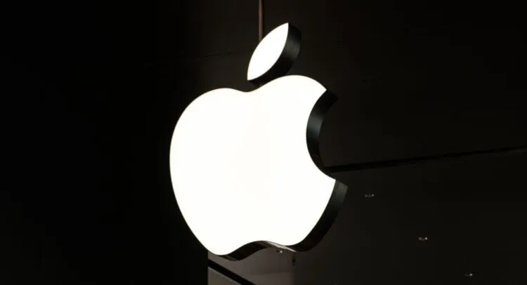 Illuminated Apple logo sign hanging in a dark environment.