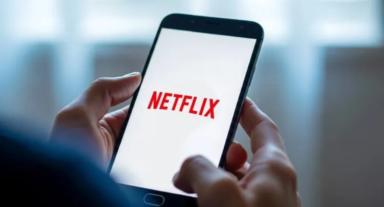 Close-up of hands holding a smartphone displaying the Netflix logo.