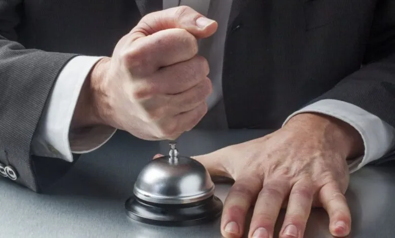Close-up of a man in a suit ringing a service bell with his fist.