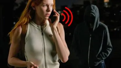 Woman on phone looking concerned as a hooded figure approaches in the dark.