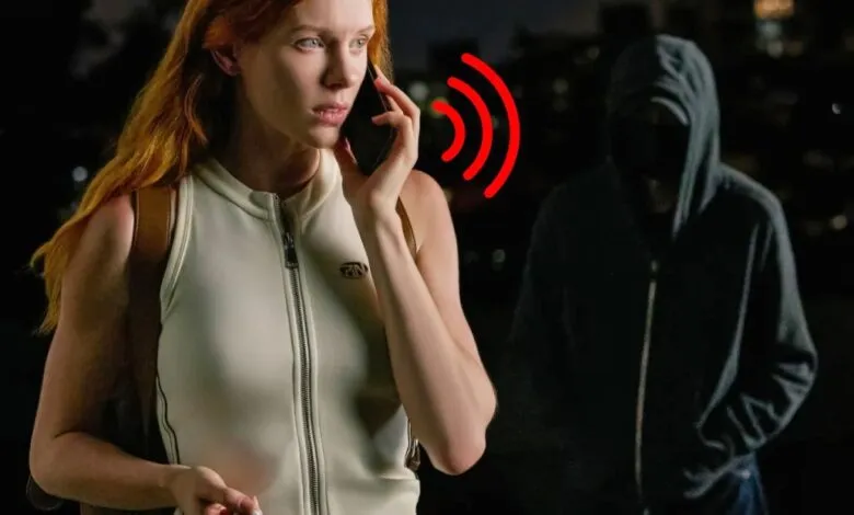 Woman on phone looking concerned as a hooded figure approaches in the dark.