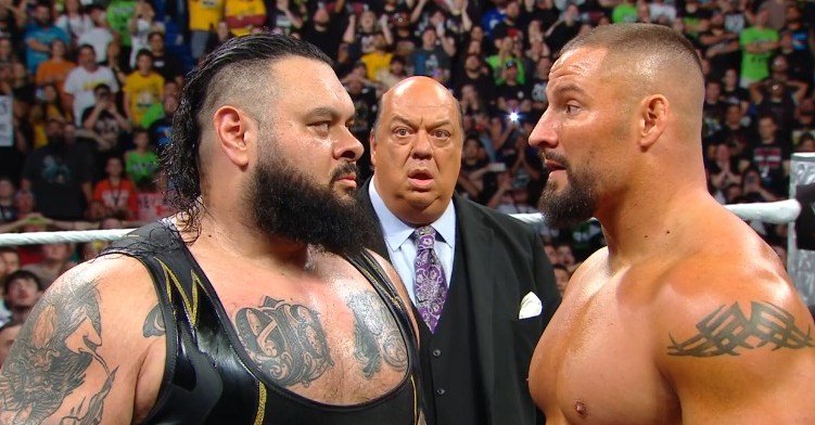 Wrestlers Sika and Roman Reigns face off with Paul Heyman in the background.