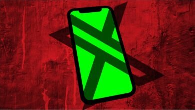 Smartphone with a green screen displaying a dark X shape against a red textured background.