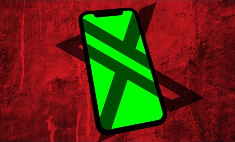 Smartphone with a green screen displaying a dark X shape against a red textured background.