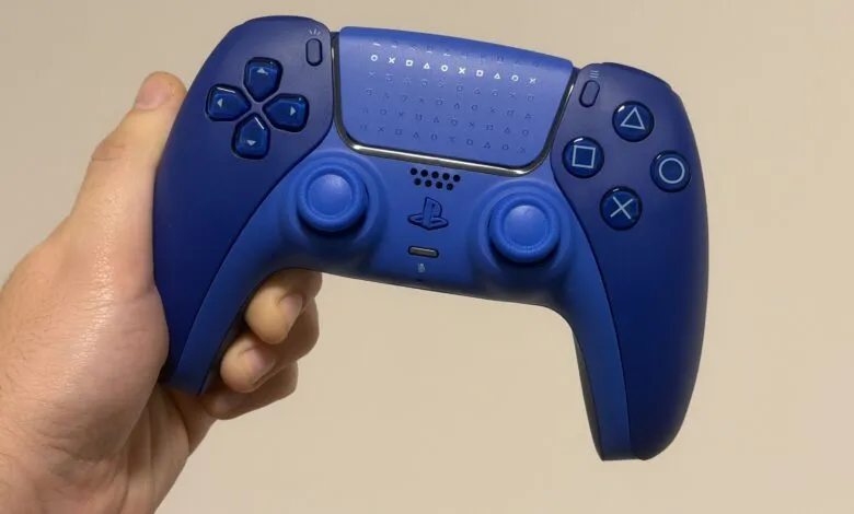 A hand holds a vibrant blue PlayStation 5 DualSense controller.