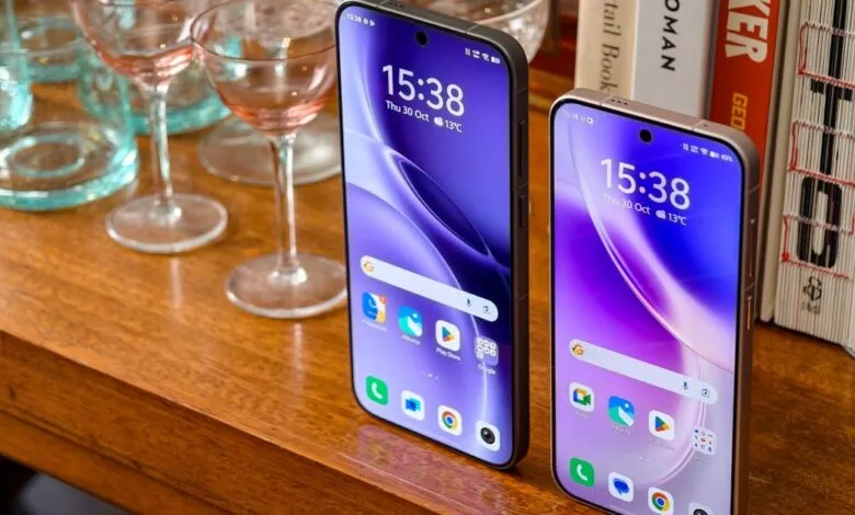 Two smartphones with purple wallpapers displayed on a wooden surface next to glassware and books.