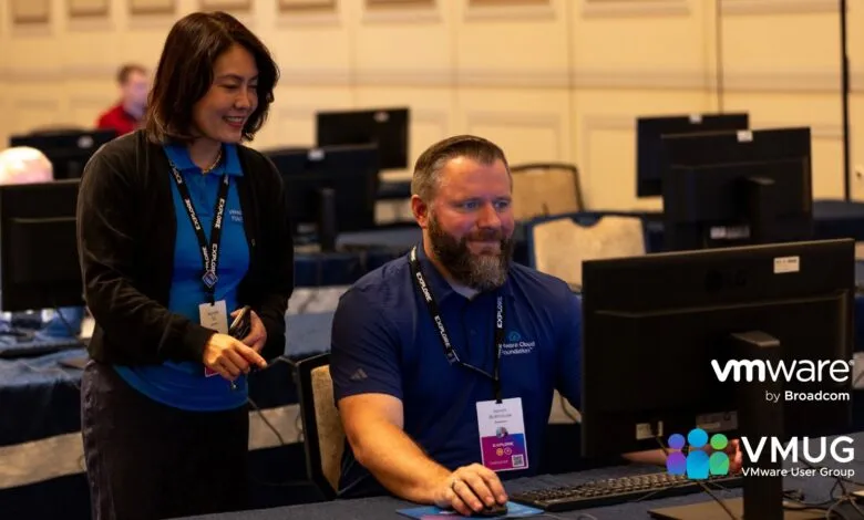 A woman in a blue shirt and black cardigan smiles while looking at a computer screen, with a man in a blue shirt seated at the same computer.