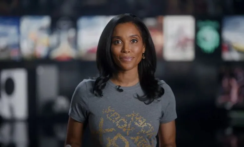 A woman with dark hair smiles at the camera, wearing a grey t-shirt with a gold graphic.