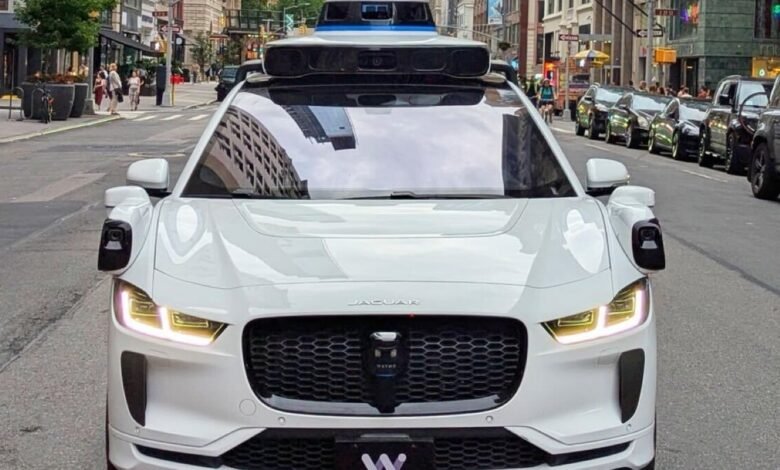 A white Waymo autonomous Jaguar I-PACE drives down a New York City street.