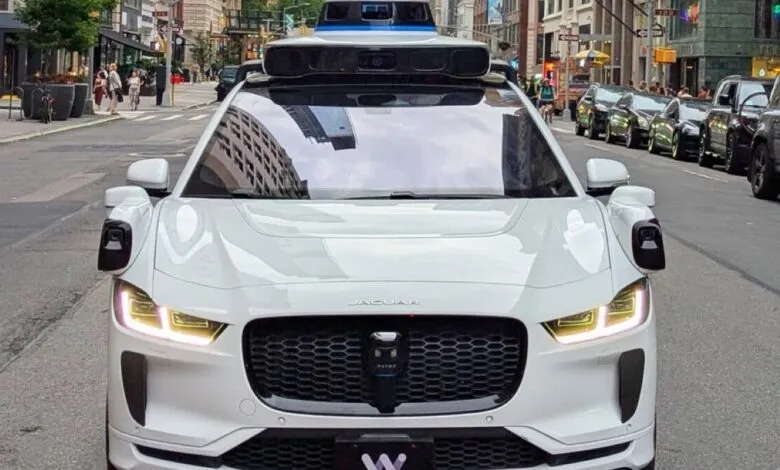 A white Waymo autonomous Jaguar I-PACE drives down a New York City street.