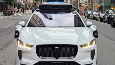 A white Waymo autonomous Jaguar I-PACE drives down a New York City street.