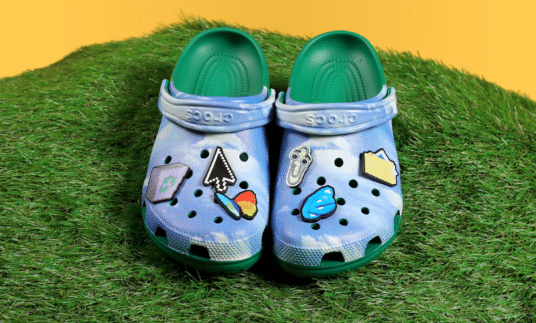 A pair of blue tie-dye Crocs with green insoles, decorated with tech-themed Jibbitz.