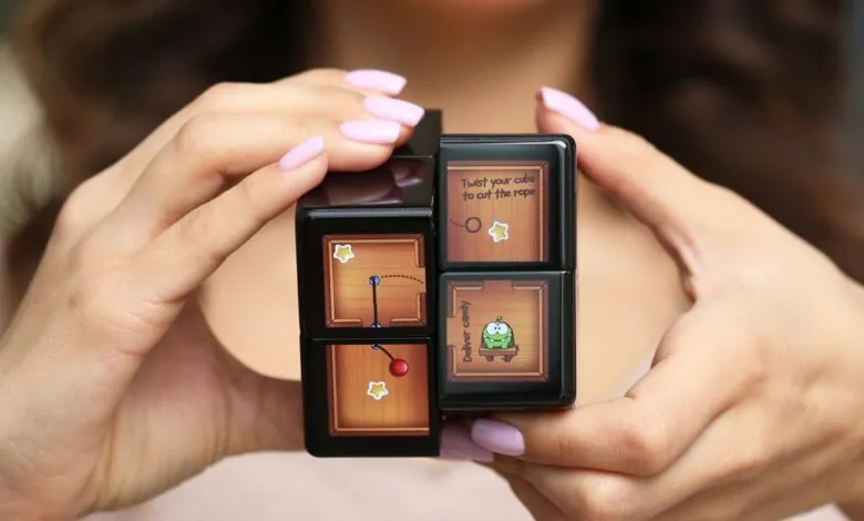 Hands holding a black cube toy with Cut the Rope game graphics.