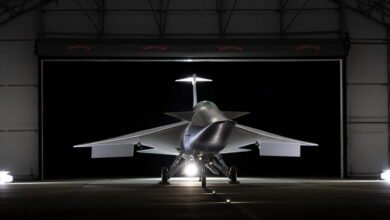 Front view of a futuristic, silver supersonic jet aircraft parked inside a dimly lit hangar.