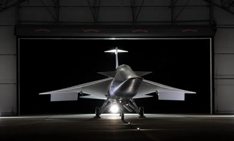 Front view of a futuristic, silver supersonic jet aircraft parked inside a dimly lit hangar.