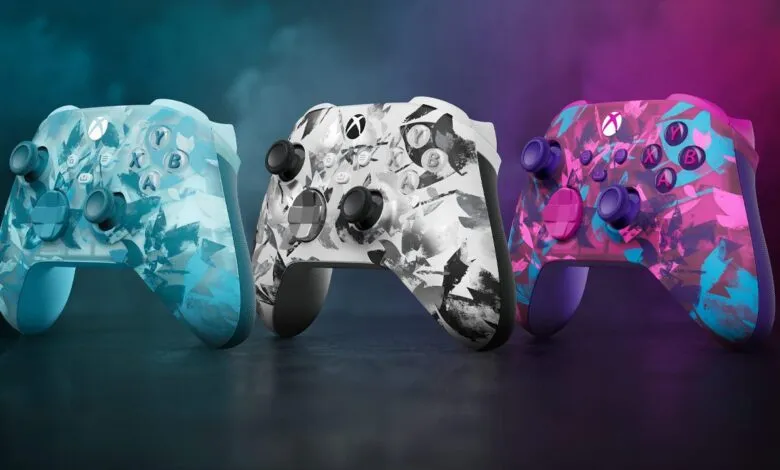 Three Xbox wireless controllers with unique abstract camouflage patterns in blue, black and white, and pink and purple.