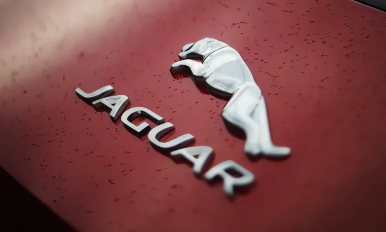 Close-up of the chrome Jaguar emblem and lettering on a red car hood.