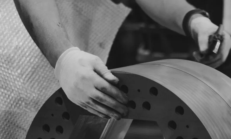 Close-up of hands in white gloves working on a large metal component with circular holes.