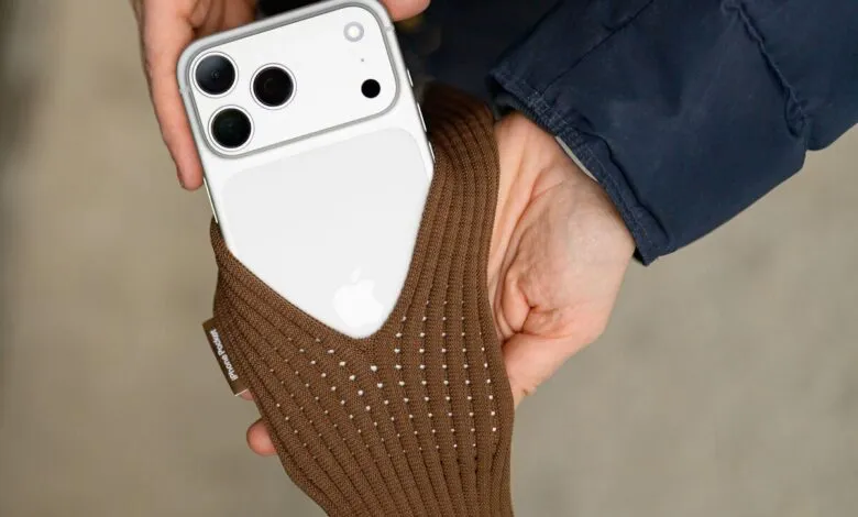 Close-up of hands holding a white iPhone with a brown knitted sleeve.