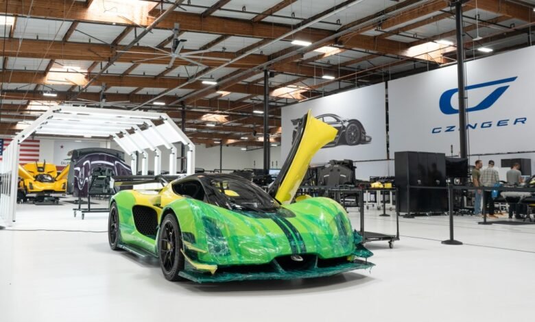 A bright green and yellow hypercar with its doors open in a modern automotive workshop.