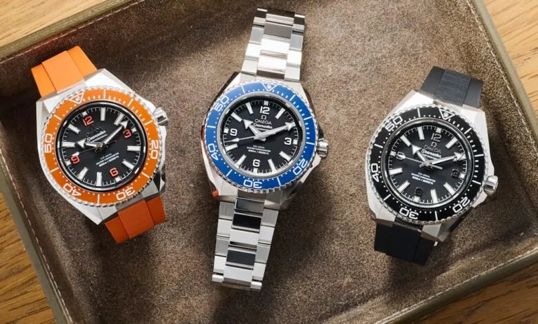 Three Omega Seamaster Planet Ocean watches with black dials and different colored bezels and straps.