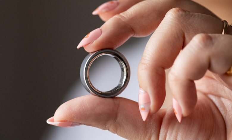 Hand holding a silver Oura Ring, showcasing its design and technology.