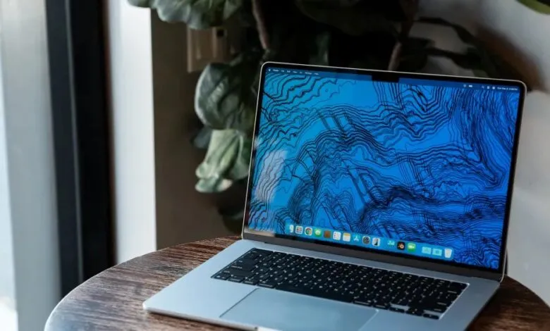 Silver MacBook Air on a wooden table with a blue topographical map wallpaper.