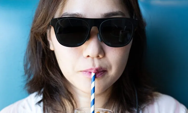 Close-up of a woman wearing black sunglasses, drinking from a striped straw.