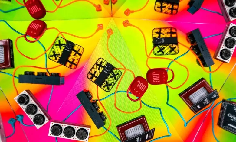 A vibrant, kaleidoscopic arrangement of electronic gadgets and cables on a neon background.