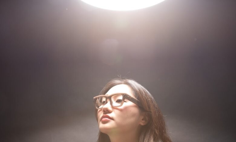 Woman wearing smart glasses with wooden frames looking upwards towards a bright light.