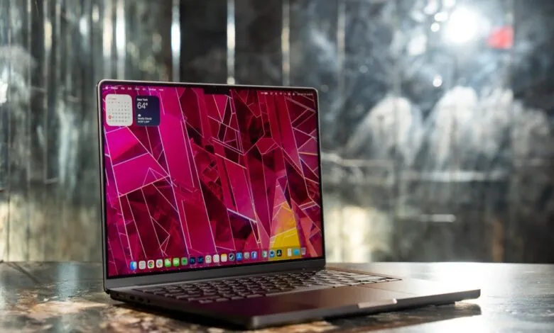 Apple MacBook Pro 14-inch laptop on a textured surface with a pink geometric wallpaper.