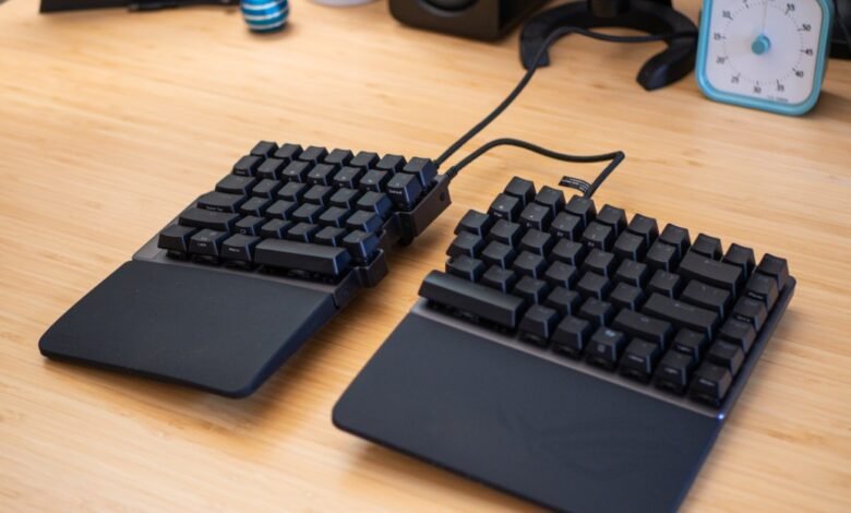 A split ergonomic keyboard with black keys and wrist rests on a wooden desk.