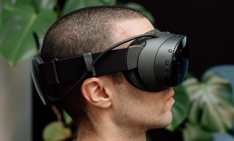Close-up profile of a man wearing a sleek black VR headset, with lush green foliage in the background.