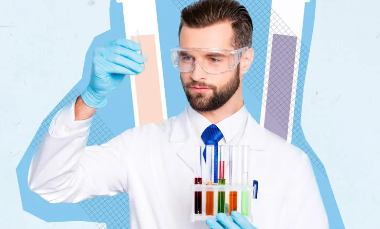 Scientist in lab coat and goggles holding test tubes with colorful liquids.