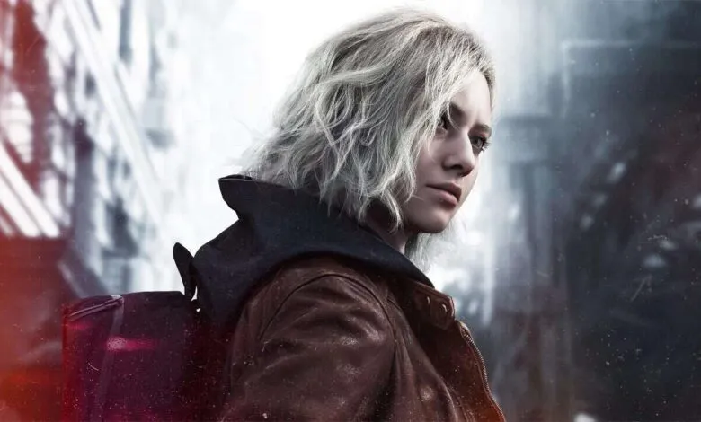 Close-up of a young woman with short, wavy blonde hair, wearing a brown leather jacket and a backpack.