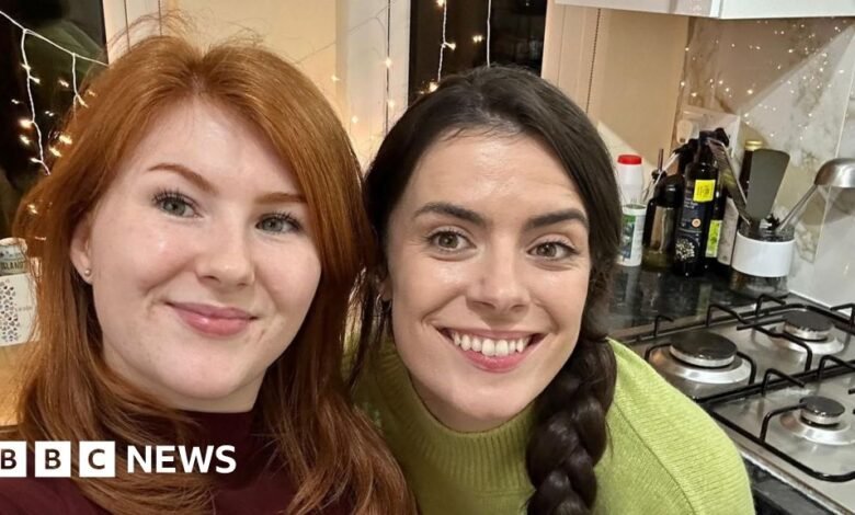 Two smiling women in a kitchen, one with red hair and the other with dark hair.