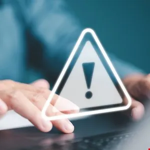 Glowing warning triangle with an exclamation mark over hands typing on a keyboard.