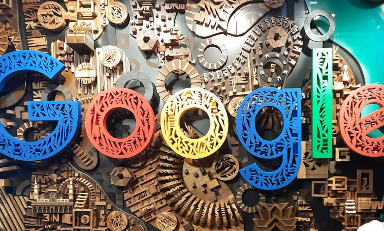 Colorful Google logo made of laser-cut wood, set against a backdrop of intricate wooden gears and structures.