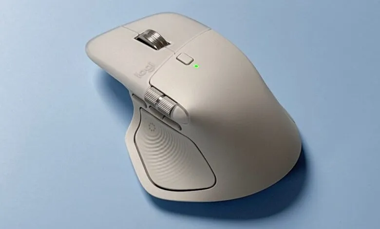 Close-up of a light gray Logitech MX Master 3S wireless mouse on a blue surface.