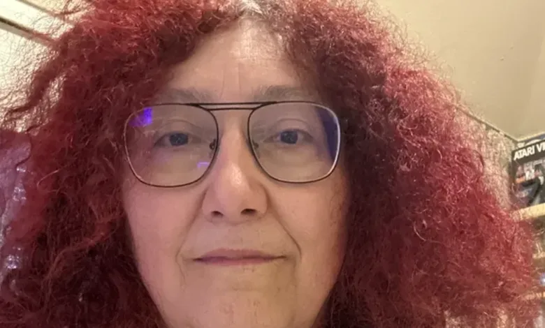 Close-up portrait of a woman with curly red hair and glasses.