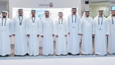 Group of men in traditional white Emirati clothing standing in front of a screen displaying energy data.