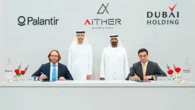 Four men in formal attire and traditional Emirati dress signing a document at a table.