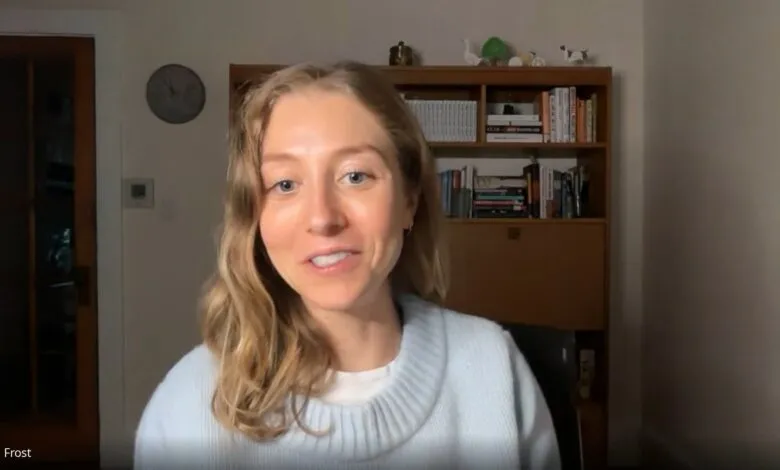 Aja Frost smiles during a video call, with a bookshelf in the background.