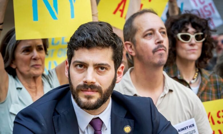 Man in suit with beard and purple tie at a protest with signs in background
