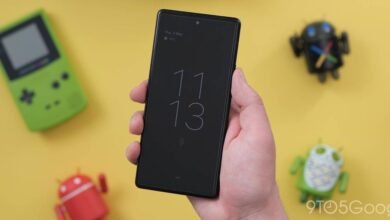 Hand holding a black smartphone displaying the time and date on its always-on display.