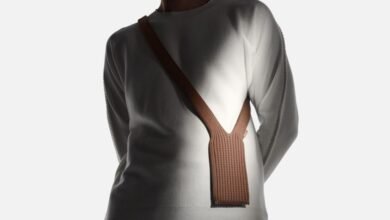 Person wearing a white long-sleeved shirt with a brown knitted phone holster across their chest.