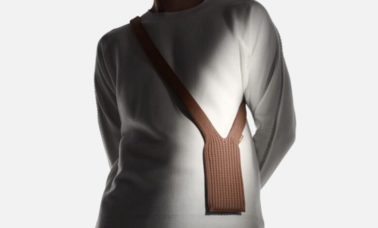 Person wearing a white long-sleeved shirt with a brown knitted phone holster across their chest.