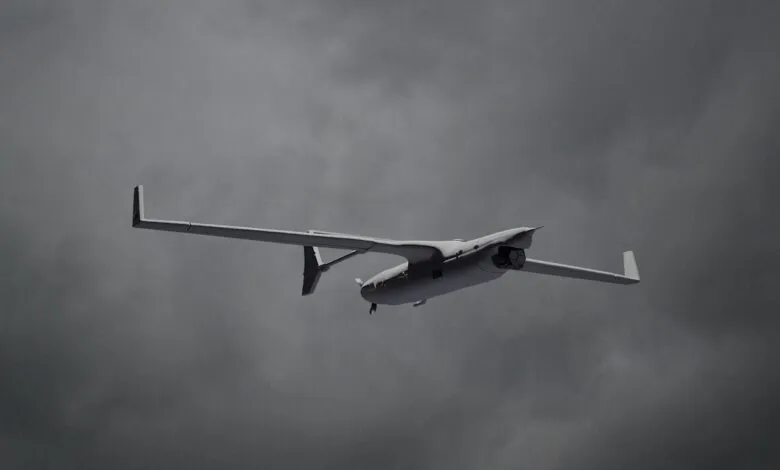 A gray unmanned aerial vehicle (UAV) with long wings flies against a cloudy sky.